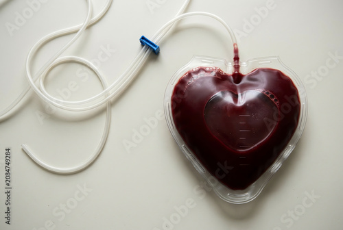 Heart-shaped blood bag with tubing isolated on a light background. Medical donation concept, healthcare, transfusion, life-saving treatment, hospital equipment, minimal composition.
