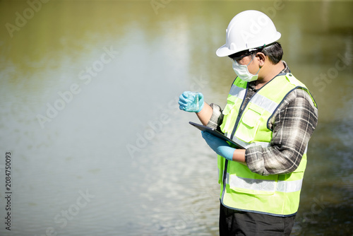 Environmental scientist testing water quality using a flask and tablet at the shoreline in a serene natural environment