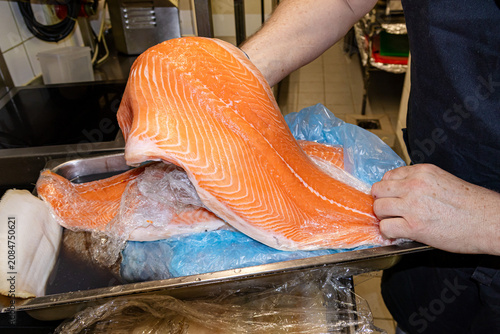 Professional chef hands holding fresh salmon fillet showing distinctive orange flesh patterns