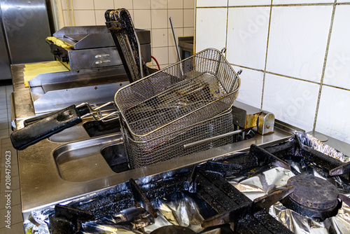 Chef handling large metal frying basket at commercial kitchen deep fryer workstation