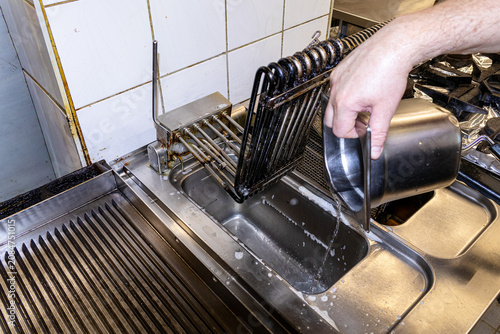  Chef pouring cooking oil into commercial deep fryer baskets during food preparation service
