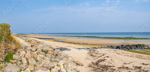 Paisaje panorámico de la Playa de Saint-Aubin-sur-Mer, en la Normandía Francesa, con cielo azul, mar en el horizonte y arena dorada en la playa con piedras, viajando en verano de 2022