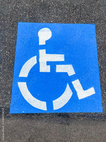 A white disabled parking symbol in a bright blue square freshly painted in natural daylight.