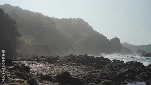 Misty Rocky Coastline with Waves Breaking over Dark Coastal Rocks, Dramatic Sea Cliffs, and Ocean Spray, Creating a Moody Atmospheric Seascape with Rugged Natural Texture