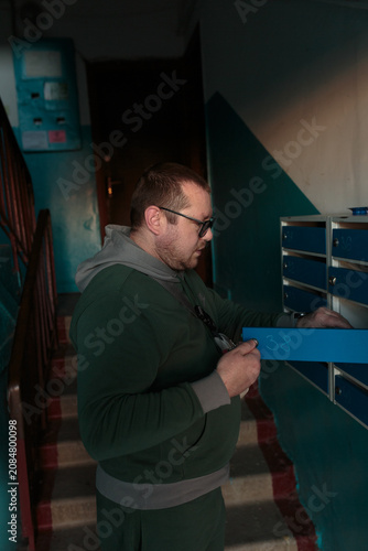 Man Checking Mailbox in Apartment Stairwell