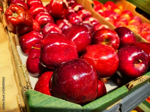 Fotografie Fresh shiny red apples fill a cardboard crate at a grocery market, piled togethe
