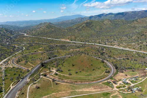 Aerial view of the Tehachapi Railroad Loop winding around a green hill in a mountainous landscape, Bear Valley Springs, California, United States.