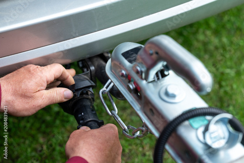 A man connects an electrical connector of trailer to a car. Male hands connect a power cable to a hitch socket, symbolizing diligence, responsibility, and technical attention