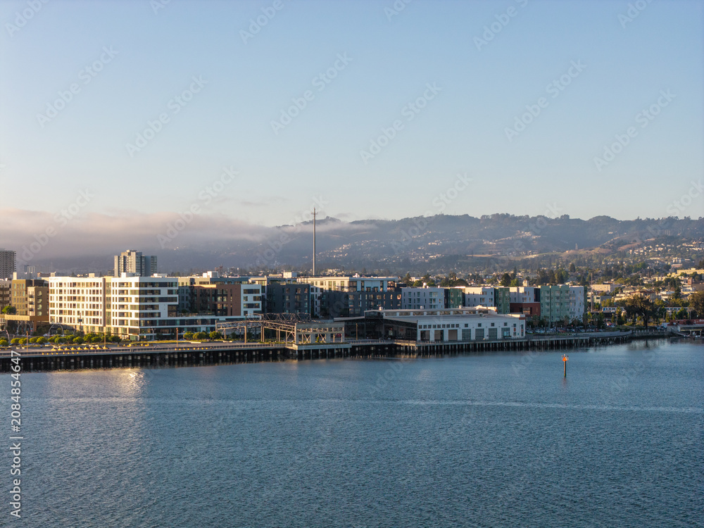 Obraz premium Oakland California waterfront showing urban development with modern residential buildings along the bay, backed by hills under a clear sky