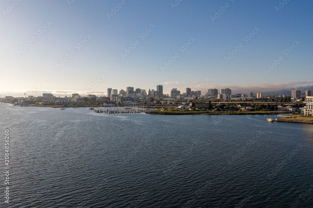 Fototapeta premium Oakland California waterfront presenting its downtown skyline with modern buildings, a bustling marina, the bay, and distant fog under a clear sky