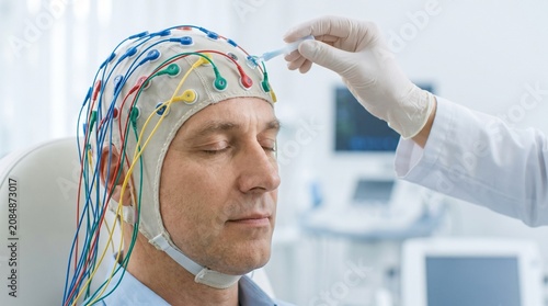 Neurology. Neurologist applying conductive gel to an EEG electrode cap on an adult patient during electroencephalography