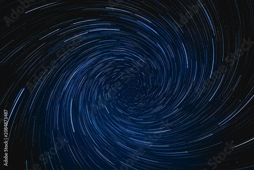 A long-exposure photograph showing spiral-shaped star trails in a dark night sky, capturing celestial rotation.