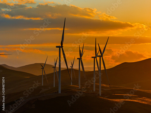 Beautiful sunset field with wind mill generators. Windmill silhouette on mountain at sunset