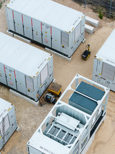 Aerial view of industrial battery energy storage system containers placed on a gravel site with electrical equipment and a small compacting machine in Suntazi, Ogre Municipality, Latvia.