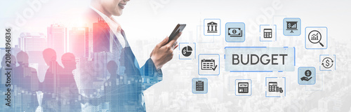 Konstfotografi Businessman in Suit Using Smartphone with Digital Budget Icons Overlay Against Urban Cityscape Background