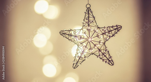 Close-up of a sparkling star-shaped Christmas ornament hanging against a soft, bokeh-filled background of warm lights.