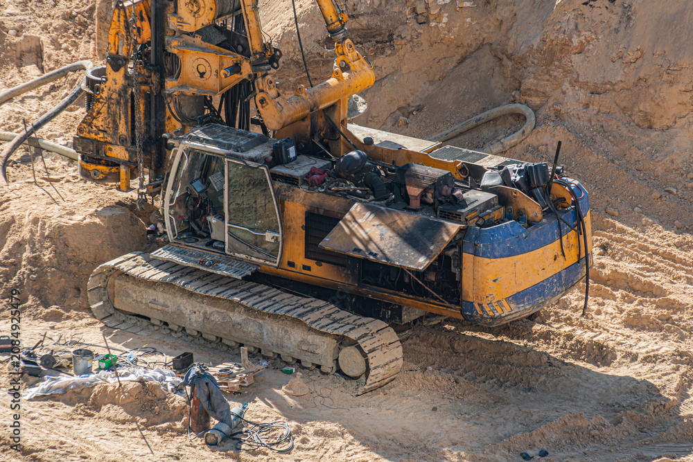 Fototapeta premium Large tracked excavator engaged in earthmoving activities, yellow and blue painted machinery, sandy open excavation site with steep slope, dusty environment, tools scattered around, heavy use tracks
