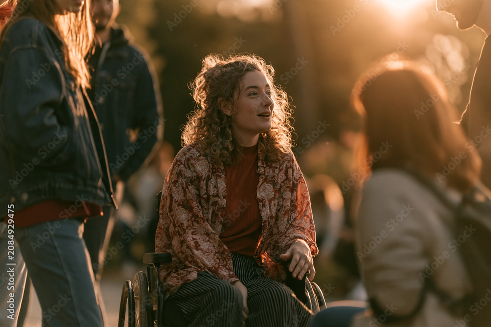 Fototapeta premium Wheelchair User Chatting with Friends in a Sunny Park, Inclusive Lifestyle