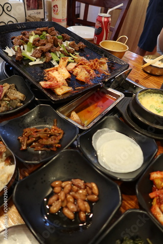 Traditional Korean barbecue featuring grilled marinated meats, fresh side dishes, and a tabletop grill. Warm, inviting dining scene showcasing authentic Korean cuisine and shared meals.