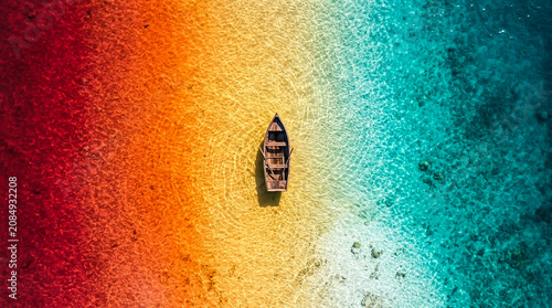 Minimalist wooden canoe floating in the center of rainbow colored tropical sea surface