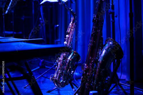Photography Close-up details of jazz instruments and musicians performing on stage under dramatic blue and purple concert lighting, featuring saxophone, piano, drumsticks and live music atmosphere