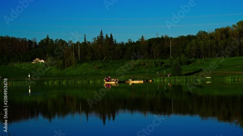 Adults and children enjoy recreational fishing from a lakeside platform during a beautiful summer sunset in Canada. A peaceful outdoor scene highlighting family leisure, nature, and lakeside recreatio