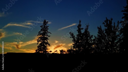 Distant views of spectacular colorful clouds illuminated by the last rays of the setting sun. Rich golden, orange, pink, and deep blue tones create a dramatic summer evening sky.