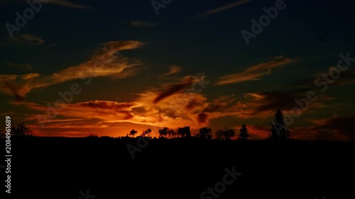 Distant views of spectacular colorful clouds illuminated by the last rays of the setting sun. Rich golden, orange, pink, and deep blue tones create a dramatic summer evening sky.