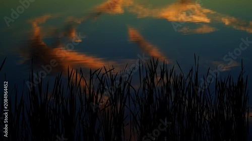 A breathtaking summer sunset reflects across the calm waters of a Canadian lake. Golden, orange, and warm evening colors create a peaceful landscape as the sun slowly disappears below the horizon.