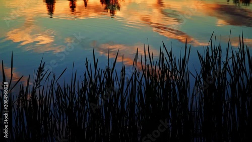 A breathtaking summer sunset reflects across the calm waters of a Canadian lake. Golden, orange, and warm evening colors create a peaceful landscape as the sun slowly disappears below the horizon.