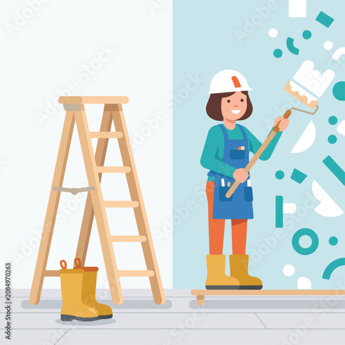 A happy female worker in a hard hat and apron uses a long-handled roller to paint a wall white, standing next to a wooden ladder in a bright room.
