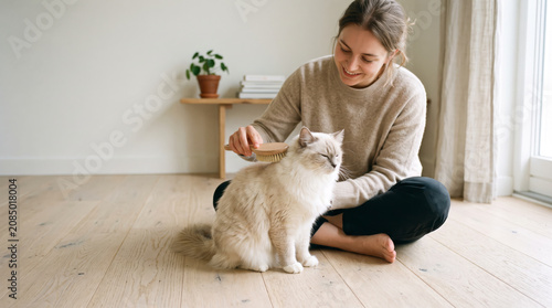 Young woman grooming her white longhair cat with a brush on the floor, pet care routine for healthy fur and reducing shedding at home