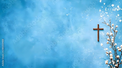 A small wooden cross next to a white cotton branch with scattered petals on a textured light blue background, symbolizing purity, peace, and spiritual tranquility with copy space.