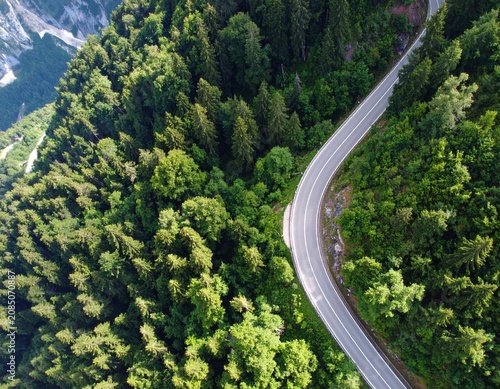 Drone view of a curved mountain road surrounded by lush forest, ideal for clean energy, EV, and green transportation concepts.