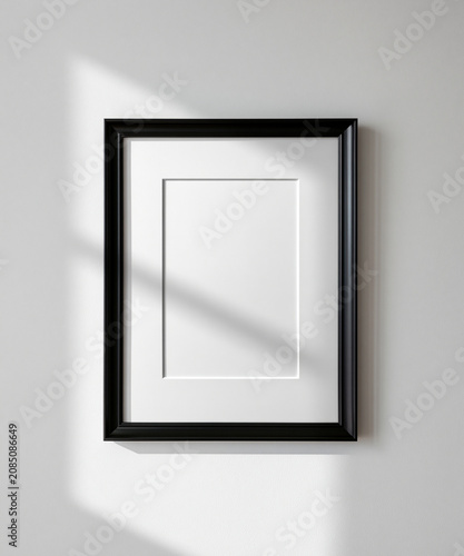 Blank vertical black poster frame mockup with white mat board border hanging on minimalist plain studio wall background for artwork presentation or photography display
