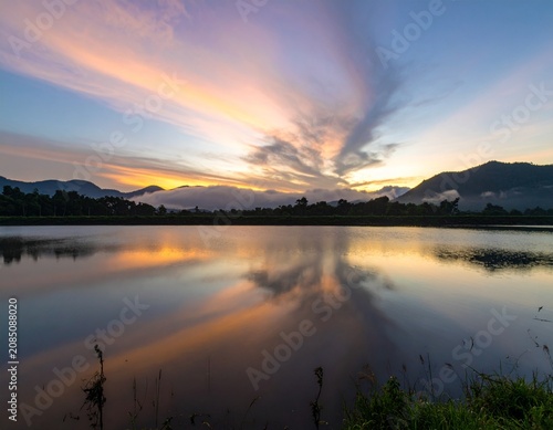 Background image of the reservoir. Beautiful sunrise or sunset sky over calm lake with reflection in surface water in the morning or evening. copy space. Lam Taphen Reservoir, Suphanburi.