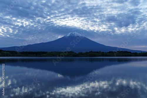Serene dawn view of Mount Fuji with dramatic rippled clouds reflected on the calm water of Lake Tanuki, Fujinomiya, Japan.