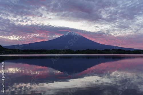 Breathtaking sunrise sky painted in vibrant pink and purple over Mount Fuji and its mirror reflection at Lake Tanuki, Japan.