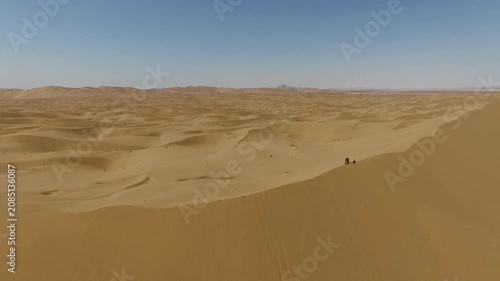 High quality aerial footage of rolling desert sand dunes with soft curves and distant mountain hints on horizon.