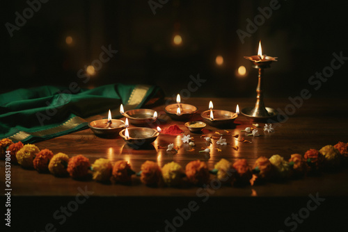 Diwali festival celebration with burning oil lamps, traditional clay diya on wooden table, marigold flower garland and brass lamp for hindu puja