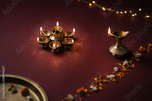 Traditional Diwali brass oil lamps with glowing flames, festive diya arrangement on dark red background, spiritual Indian celebration with flower petals