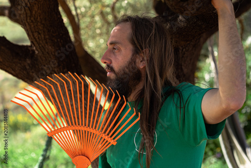 Man with long hair holding rake gardening outdoors