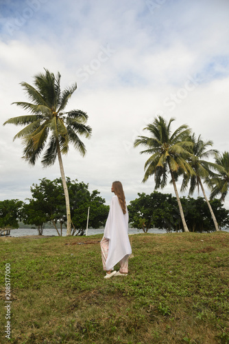 Woman in White Dress Walking on Green Grass in Tropical Landscape