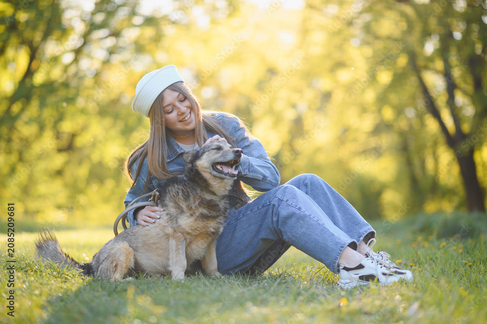 Fototapeta premium Young woman petting dog in park at sunset