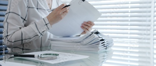 Financial auditor reviewing company documents, checking tax compliance reporting, conducting a detailed investigation, and thoroughly analyzing business paperwork for legal adherence
