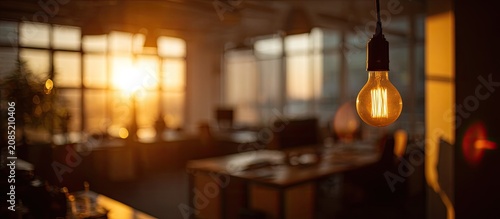 A vintage bulb glows warmly in an office at sunset, casting soft light