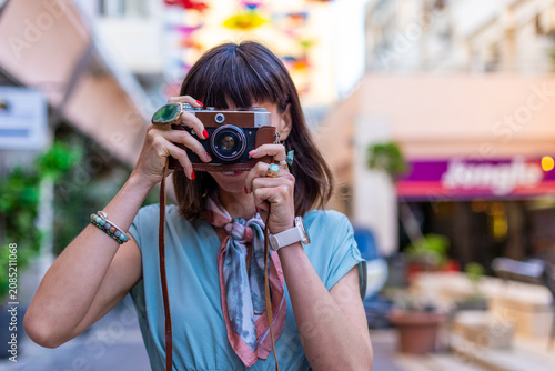 Fotografie Close-up of a dark-haired woman holding a vintage camera near her face, looking through the viewfinder with focused expression