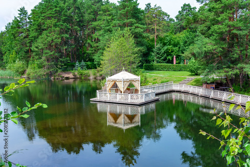 A gazebo on a wooden platform in a lake surrounded by a forest.
