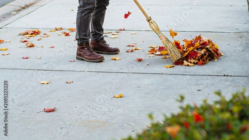 Person sweeping autumn leaves from sidewalk during seasonal cleanup