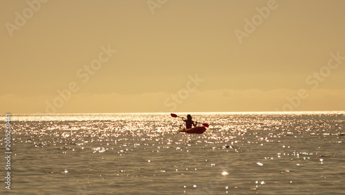 Kayaking sunset ocean solitary person paddling red kayak across glittering water during golden hour